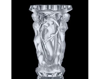 May include: A clear, frosted glass vase featuring a relief sculpture of three figures with flowing drapery encircling the exterior. The vessel has a wide, scalloped rim and a faceted base, showcasing intricate detailing on the human forms.