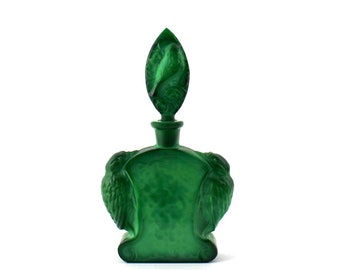 May include: A green glass bottle with a bird design on the stopper. The bottle has a textured surface and is shaped like a bird.