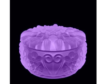 May include: A purple glass trinket box with a floral design. The lid features a large flower with smaller flowers and swirls around the sides.