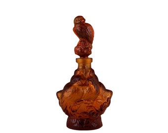 May include: Amber glass bottle with a bird-shaped stopper. The bottle is decorated with a design of birds and leaves.