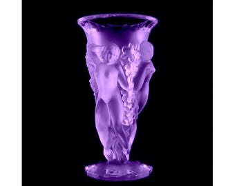May include: A purple glass vase with a sculpted design of a woman and grapes. The vase has a wide mouth and a narrow base.