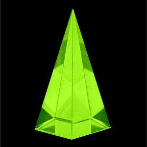 May include: A neon green, geometric pyramid-shaped object. The pyramid has a flat base and sharply angled sides that converge at a point. The object is made of a translucent material and is set against a black background.