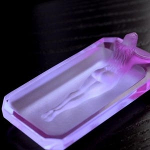 K&ouml;nnte beinhalten: Ein Aschenbecher aus violettem Glas mit einem erhabenen Design einer liegenden Person.