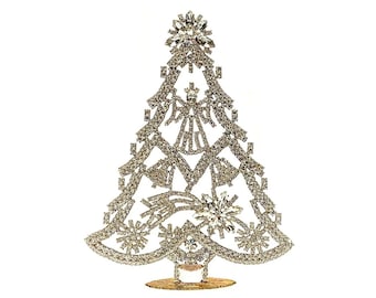 May include: A silver-toned, triangular Christmas tree ornament encrusted with clear rhinestones. The design features a star at the top, an angel figure in the center, and snowflake and shooting star motifs throughout the openwork metal frame.