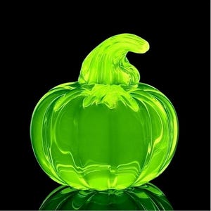 Peut inclure: Une citrouille en verre vert vif avec une tige incurvée. La citrouille est lisse et réfléchissante, avec une finition brillante. Le fond noir met en valeur la couleur et la forme vives de la citrouille. Un objet décoratif pour l'automne.