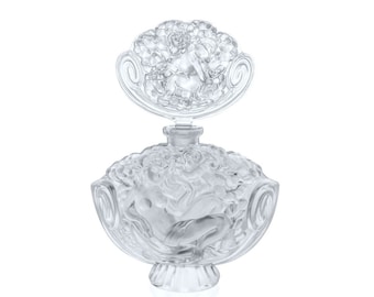May include: A clear glass perfume bottle with a detailed, ornate design. The bottle features a sculpted figure of a woman and a floral motif. The bottle has a clear glass stopper with a similar design.