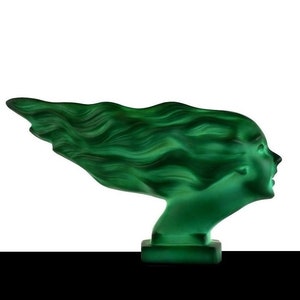 Puede incluir: Una escultura de vidrio verde de la cabeza de una mujer con el pelo suelto. La escultura está en un estilo art déco estilizado.