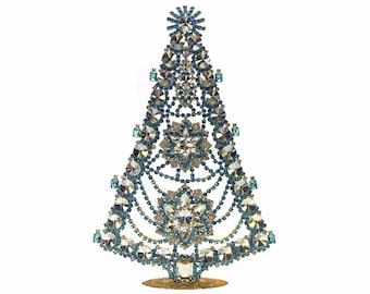 May include: A decorative Christmas tree made of clear and blue crystals. The tree features a star at the top and is set on a gold-colored base. The crystals are arranged in a festive, elegant design.