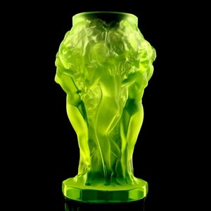May include: A green glass vase with a design of three women standing together. The vase is made of frosted glass and has a textured surface.