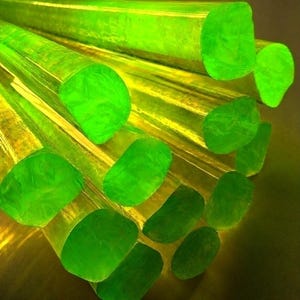 Puede incluir: Un manojo de varillas cilíndricas translúcidas de color verde neón con superficies lisas y reflectantes. Las varillas están dispuestas en un grupo, mostrando su vibrante color verde lima semitransparente y sus secciones transversales redondeadas.