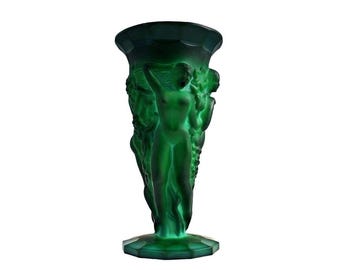 Puede incluir: Un jarrón de vidrio verde con un diseño esculpido de tres mujeres. El jarrón tiene una boca ancha y una base acampanada.