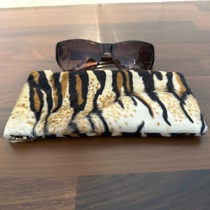 May include: A brown and black zebra print glasses case with a pair of brown sunglasses on top of it.
