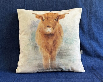 May include: A brown and white Highland cow cushion with a watercolor background. The cushion is made of a soft, natural fabric and features a realistic image of the cow.