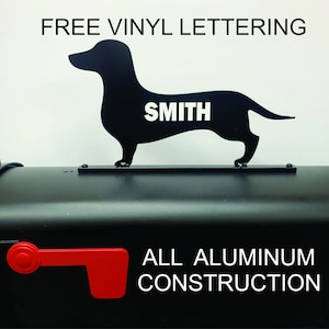 May include: Black metal dachshund mailbox topper with the name "SMITH" in white vinyl lettering. The topper is mounted on a black mailbox with a red flag. The text "ALL ALUMINUM CONSTRUCTION" is printed on the mailbox.