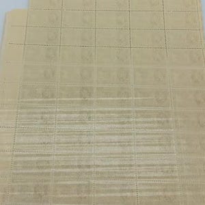 以下が含まれることがあります： グリッド状に配置されたベージュ色の郵便切手の大きな長方形のシート。各切手はミシン目で区切られており、わずかに濃いベージュ色で印刷されたかすかな円形のエンブレムデザインが特徴です。