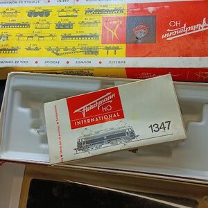 May include: Two rectangular Fleischmann HO model train construction kit boxes with red and yellow branding, featuring technical diagrams and logos. A smaller white box labeled Fleischmann HO International 1347 with a train illustration sits inside.