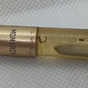 May include: A gold-toned ballpoint pen featuring a metallic barrel with the text MONARCH printed on it. The upper section is a clear, liquid-filled chamber containing a miniature floating ship model, finished with a gold-toned clip and tip.