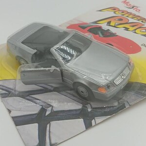 May include: A silver die-cast model car with an open door, displayed on its original packaging. The packaging features the words "Maisto POWER RACERS" and an image of a red sports car. The model car has black interior and orange headlights.