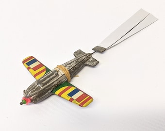 Puede incluir: Un avión de juguete vintage hecho de metal con un cuerpo gris y alas coloridas. Las alas están pintadas con rayas rojas, amarillas, azules y verdes. El avión tiene una cuerda atada a la parte posterior para tirar.