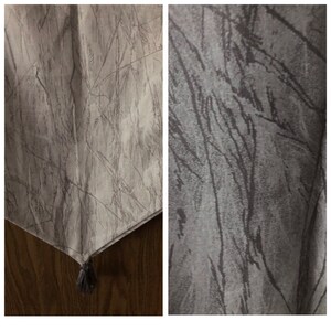 May include: A light gray table runner with a textured, abstract design. The runner features a pattern of thin, dark gray lines resembling branches or veins. A small gray tassel hangs from the corner. The fabric appears to be soft and slightly reflective.