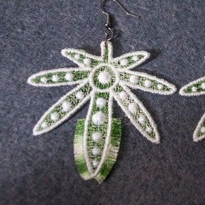 May include: A pair of green and white lace earrings shaped like a marijuana leaf. The earrings have a silver hook.