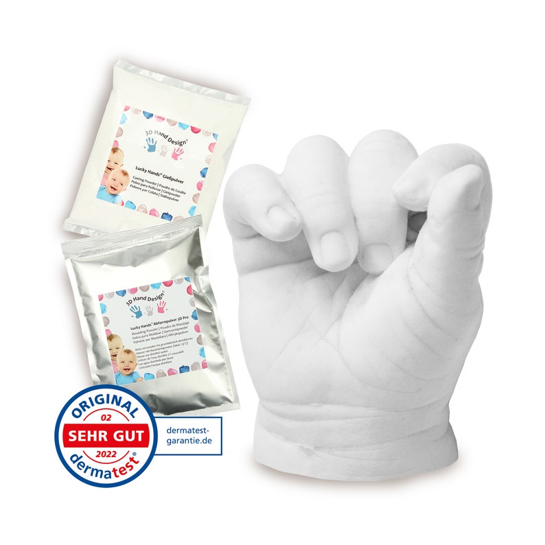 May include: Two white packets of 3D Hand Design Lucky Hand molding powder with a white plaster hand cast of a baby's hand in a fist. The packets have a blue and pink design with a picture of a baby's hand and the text "Lucky Hand Goldpulver". The plaster cast is on a white background. The image also includes a "Dermatest" seal with the text "Original Sehr Gut 2022 Dermatest".