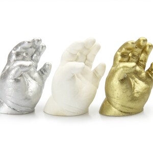 May include: Three baby hand casts, one silver, one white, and one gold.