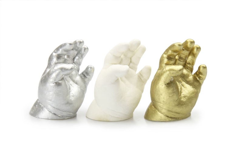 May include: Three baby hand casts, one silver, one white, and one gold.