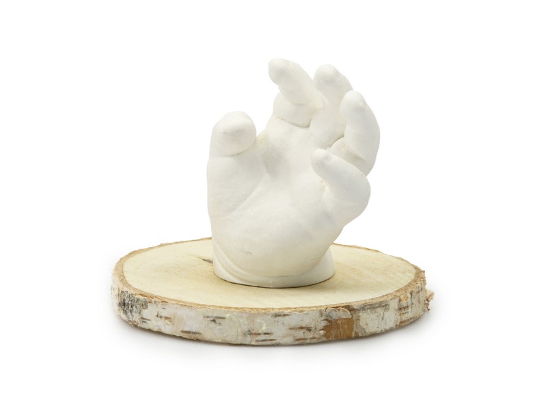May include: A white plaster hand cast on a wooden base. The hand is in a relaxed position with the fingers slightly curled.