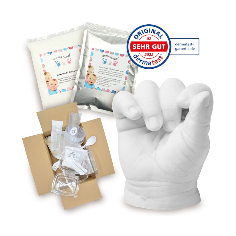 May include: A 3D hand casting kit with two bags of casting powder, a clear plastic container, a spoon, a syringe, and a white plaster hand cast. The kit is in a brown cardboard box. The box is open and the contents are visible. The kit is labeled "3D Hand Design" and "Lucky Hands - Handprint & Footprint Kit".