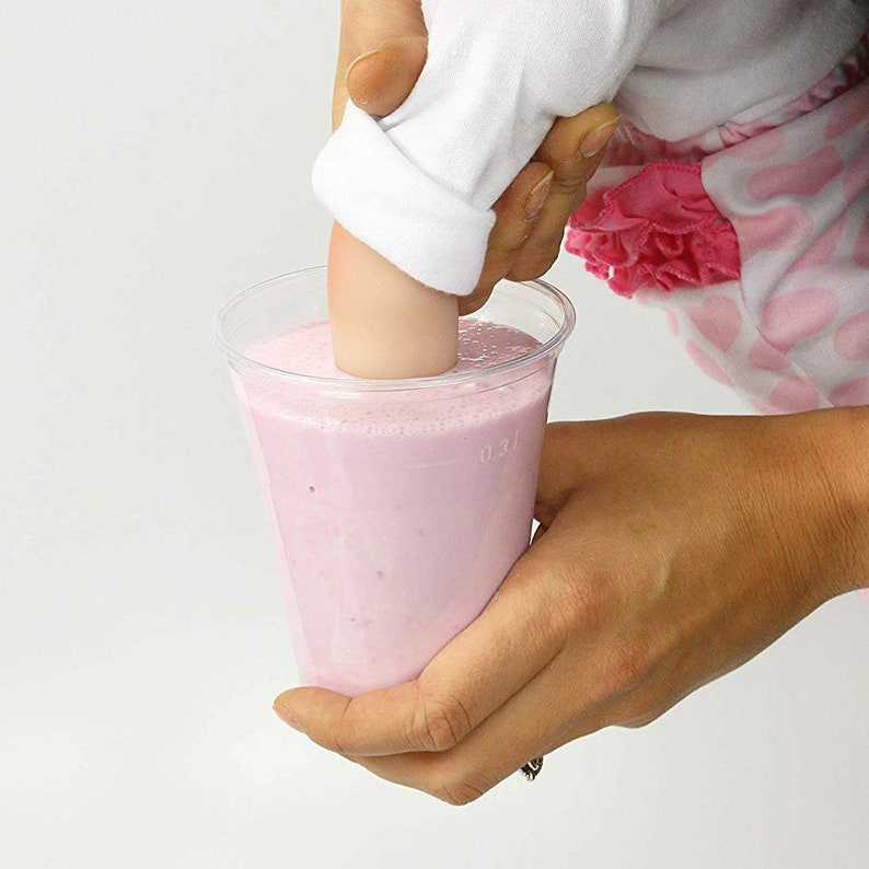 May include: A hand reaches into a clear plastic cup filled with pink liquid. The liquid is thick and creamy, and the hand is pushing down on the surface of the liquid.