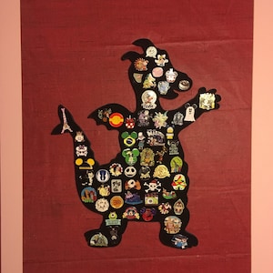 May include: A black silhouette of a dragon with a long tail, filled with colorful pins and buttons. The dragon is on a red background.