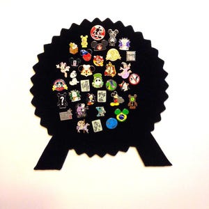 May include: A black felt pin board shaped like a circle with a ribbon at the bottom. The board is filled with various Disney character pins, including Mickey Mouse, Minnie Mouse, Donald Duck, Goofy, and Pluto.