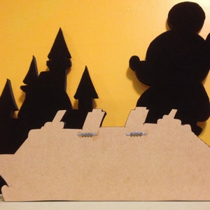 May include: A brown wooden silhouette of a cruise ship with black silhouettes of Mickey Mouse and a castle behind it.