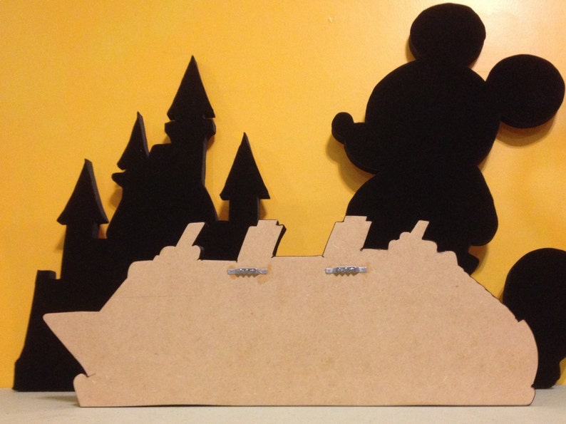 May include: A brown wooden silhouette of a cruise ship with black silhouettes of Mickey Mouse and a castle behind it.