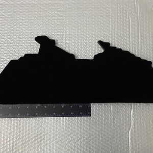 May include: Black silhouette of a cruise ship, cut out of a material like wood or cardboard. The silhouette is about 12 inches long.