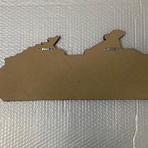 May include: A brown wooden cutout of a cruise ship with two metal hangers on the back.