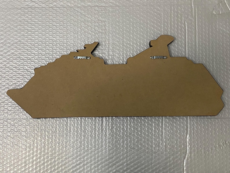 May include: A brown wooden cutout of a cruise ship with two metal hangers on the back.