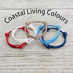 May include: Four braided rope bracelets in red, white, blue, and brown. The bracelets are tied together in a knot and the text "Coastal Living Colours" is written above them.