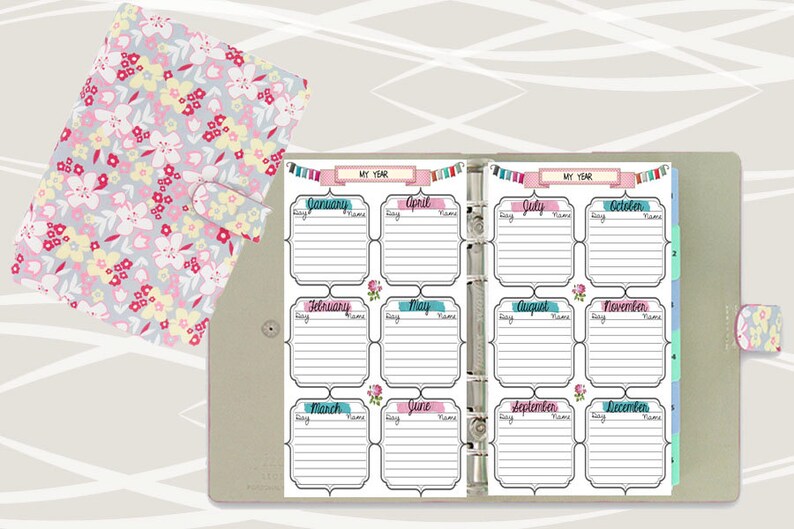May include: A white planner with a floral design on the cover. The planner is open to a page with a calendar layout for each month of the year. The months are labeled with colorful banners and the days are listed in columns. The planner is designed for organizing and tracking events and appointments.