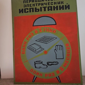 May include: Vintage Soviet sign in Russian, with a red and green design. The sign has a clock-like layout with illustrations of safety equipment and the text "PERIODIC ELECTRICAL TESTS".