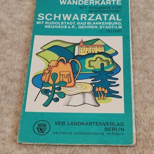 May include: A vintage German map titled "Wanderkarte Schwarzatal" with a colorful illustration of a backpack, trees, and a building. The map has a teal cover with white text. It is from VEB Landkartenverlag Berlin.