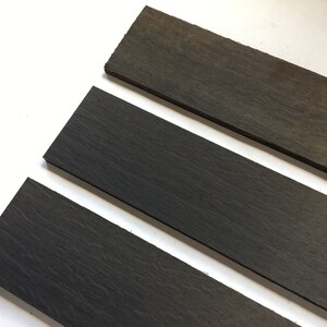 May include: Three dark gray wooden strips, arranged in a staggered pattern, on a white surface.