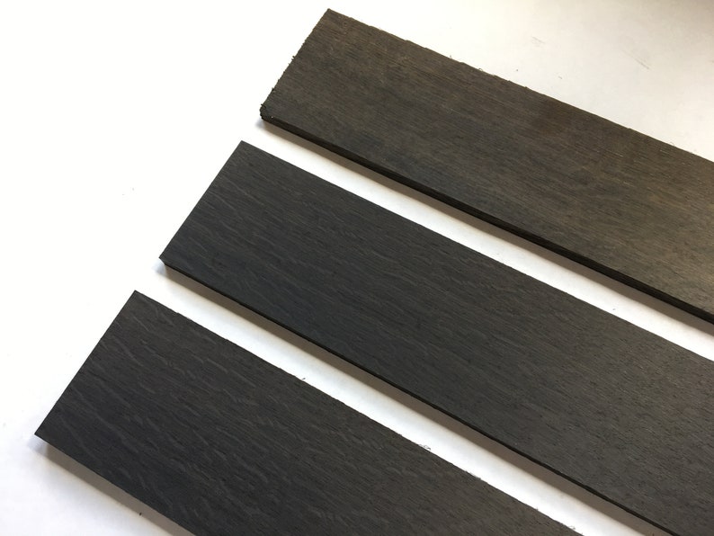 May include: Three dark gray wooden strips, arranged in a staggered pattern, on a white surface.