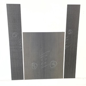 May include: Four pieces of gray wood, arranged to form a shape. Two long, narrow pieces stand vertically, flanking a wider, rectangular piece. A third rectangular piece is centered below the vertical pieces. Each piece has a number 3 written on it.