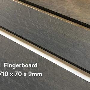 May include: A dark gray wooden fingerboard for a musical instrument, measuring 710 x 70 x 9 mm.