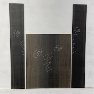 May include: A collection of dark wood pieces, likely for woodworking projects. The pieces are rectangular, with visible wood grain and markings in white. The wood has a deep, rich color, and the arrangement suggests they are for a specific craft or design.