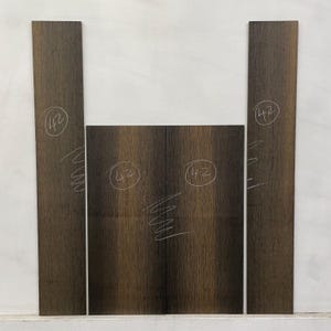 May include: A collection of dark brown wood panels, likely for woodworking projects. The panels have a vertical grain pattern and are marked with the number "42" in white. The wood has a natural, textured appearance, suggesting it is unfinished.