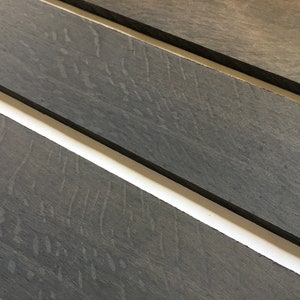 May include: Three pieces of dark gray wood with a wood grain pattern. The wood is smooth and has a matte finish.