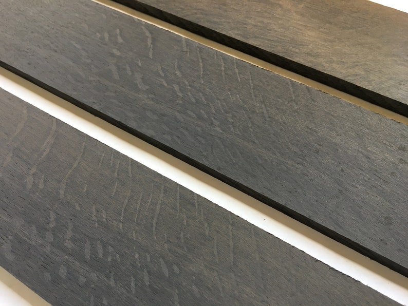 May include: Three pieces of dark gray wood with a wood grain pattern. The wood is smooth and has a matte finish.